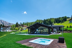 Une maison moderne dotée d’un patio entièrement vitré, d’un jacuzzi et offrant une vue sur un paysage montagneux.