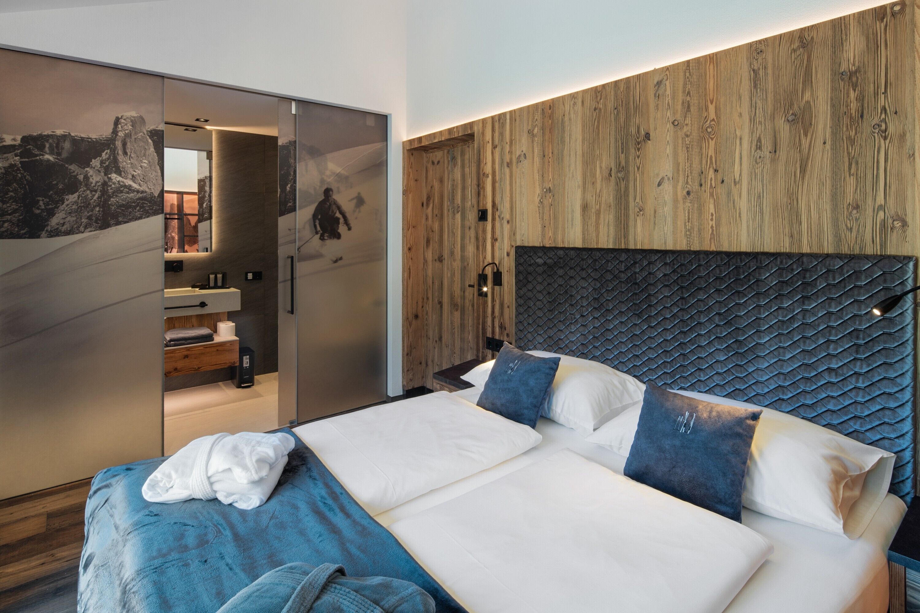 Quarto moderno com uma cama grande, cabeceira de madeira e porta deslizante que dá para um banheiro.