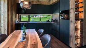 A modern kitchen with a wooden table, chairs, a potted plant, and wine glasses on shelves. - Chalet 'Ski' on the slopes with mountain view, private terrace, and Wi-Fi (Selva di Val Gardena)