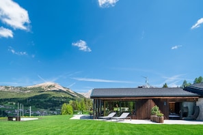 Une maison moderne dotée d’un patio, offrant une vue sur les montagnes et s’ouvrant sur un ciel dégagé.