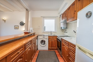 A compact kitchen with wooden cabinets, a washing machine, a coffee maker, and a window.