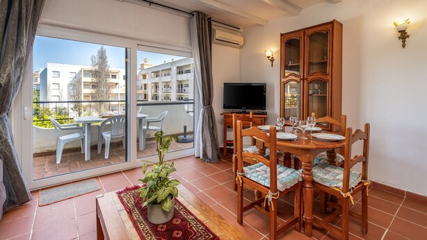 A room with a balcony, a dining table set with plates and glasses, a television, and a cabinet with glass doors. - Apartment 'Casa Doce' with Shared Pool, Wi-Fi and Air Conditioning (Alvor)