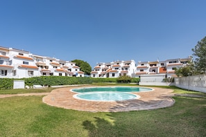 A residential area with white buildings, a circular swimming pool, and a clear blue sky.
