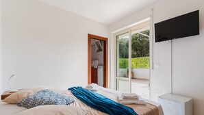 A bedroom with a bed, a TV, a mini-fridge, and a sliding glass door to a balcony. - Room 'Cassiopea' with Shared Terrace, Wi-Fi, and Air Conditioning (Otranto)