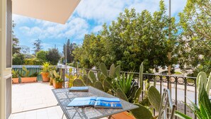 A balcony with potted plants, a metal table with a magazine, and a view of the street and buildings. - Room 'Berenice' with Shared Terrace, Wi-Fi, and Air Conditioning (Otranto)
