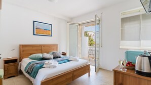 A bedroom with a wooden bed, a nightstand, a bedside table, a window with a view, and a kitchenette area with a kettle. - 'Fenice' Room with Shared Terrace, Wi-Fi, and Air Conditioning (Otranto)