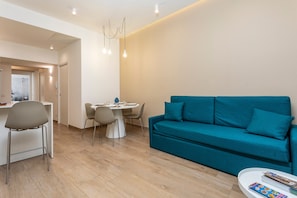 A modern living room with a teal sofa, a dining table with chairs, and a white coffee table.