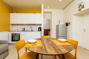 Una cocina compacta con armarios blancos, una mesa de comedor de madera con sillas amarillas y un refrigerador a la vista.