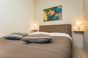 Una cama bien hecha con un cabecero marrón, dos lámparas fijadas a la pared y una obra de arte abstracta en la pared.