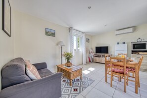 A living room with a sofa, a wooden coffee table, a dining table with chairs, a TV, and a refrigerator.