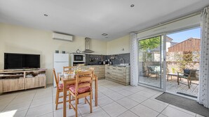 Une cuisine moderne avec un coin repas, un téléviseur et une porte-fenêtre coulissante donnant sur une terrasse extérieure.