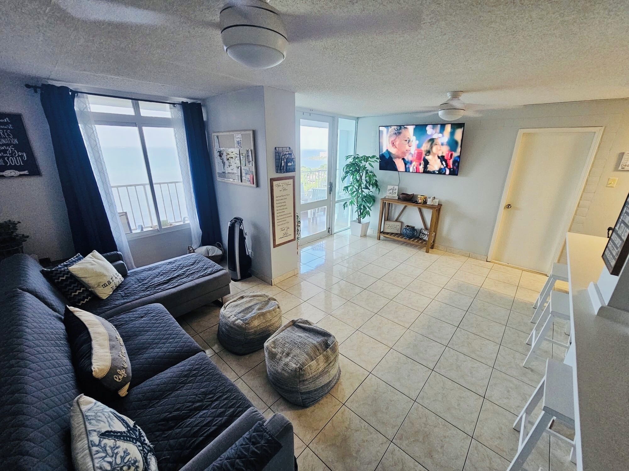 Ein Wohnzimmer mit einer Couch, Hocker, einem Fernseher und einer Zimmerpflanze.