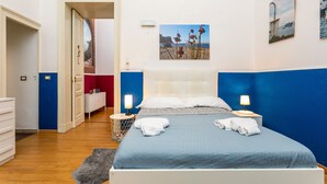 Une chambre à coucher comprenant un lit, des tables de chevet, une commode, une coiffeuse, une porte et un mur orné d’un tableau.