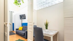 Une pièce comprenant un canapé, une table, une chaise, un téléviseur et une plante.