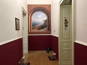 Un pasillo con un mural de paisaje costero, una puerta verde y una pequeña mesa con un florero.