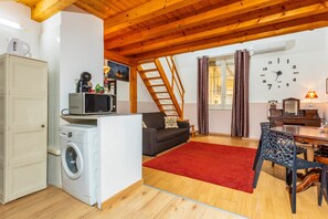 Un espacio habitable compacto con lavadora, microondas, sofá, mesa de comedor y una alfombra roja.