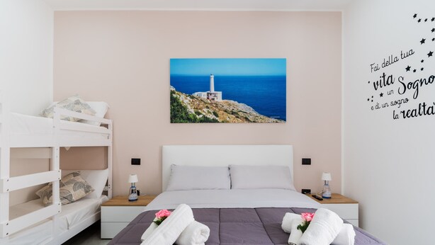 A bedroom with a bunk bed, a large bed with a purple bedspread, two bedside tables with lamps, a wall-mounted picture of a lighthouse, and a motivational quote. - 'Luxury 12 - Room Aurora' with Shared Terrace, Wi-Fi and Air Conditioning (Tuglie)