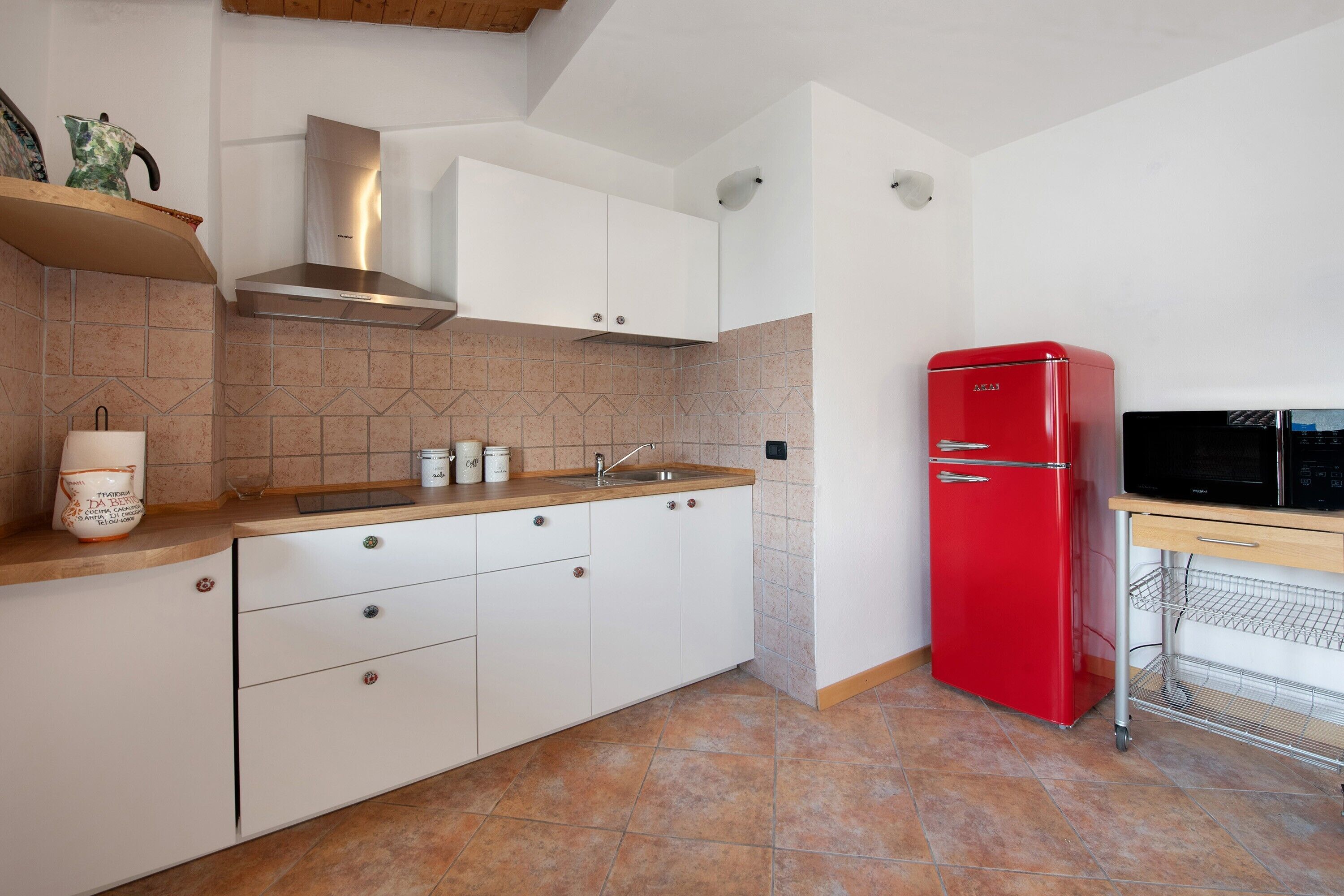 Une cuisine avec des meubles blancs, un réfrigérateur rouge et un four à micro-ondes posé sur un plan de travail en bois.