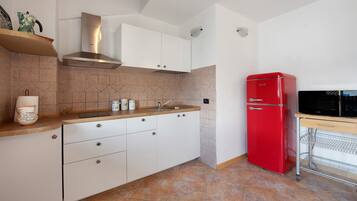A kitchen with white cabinets, a red refrigerator, and a microwave on a wooden countertop.