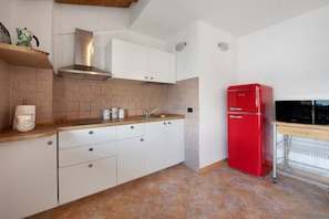 A kitchen with white cabinets, a red refrigerator, and a microwave on a wooden countertop.