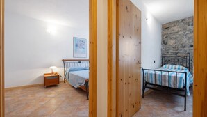 Une chambre à coucher avec un lit, une table de chevet, une lampe, un mur en pierre et une porte en bois.