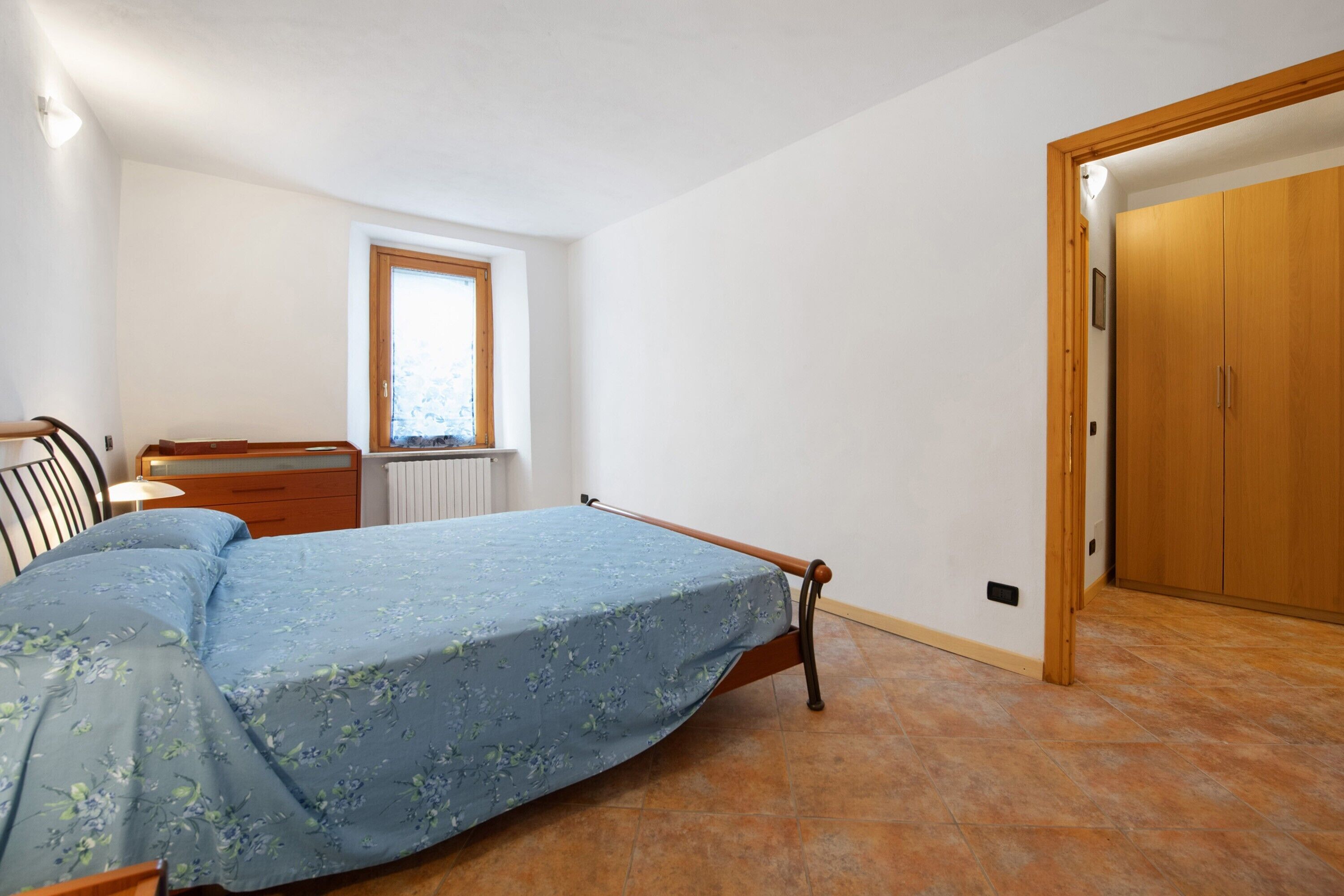 Een slaapkamer met een bed, een houten dressoir, een raam en een deur.