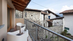 Un balcon avec des chaises blanches, un mur en pierre et une vue sur les bâtiments voisins.
