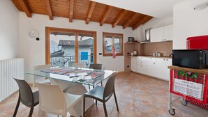 Un coin repas avec une table en verre, des chaises, une horloge et une vue sur un balcon doté d’une balustrade.