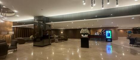 A spacious lobby with a reception desk, seating area, and a large digital screen.