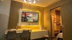 A modern dining area with a TV mounted on the wall, a chandelier, and a round table with a remote control.