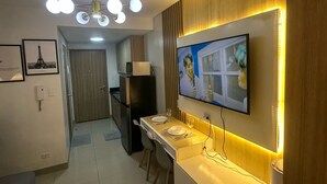 A modern kitchen with a TV mounted on the wall, a dining area with a table and chairs, and a ceiling light fixture.