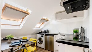 Eine kompakte Küche mit integrierter Waschmaschine und Trockner, einer schwarzen Arbeitsplatte und einem Essbereich mit gelben Stühlen und einem Tisch.