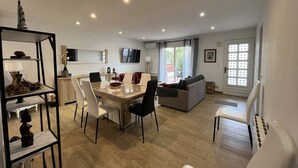 A modern living room with a dining area, a sofa, and a TV mounted on the wall. - Charming single-story villa with 3 bedrooms, tastefully decorated, beautiful exterior. (CANET PLAGE)