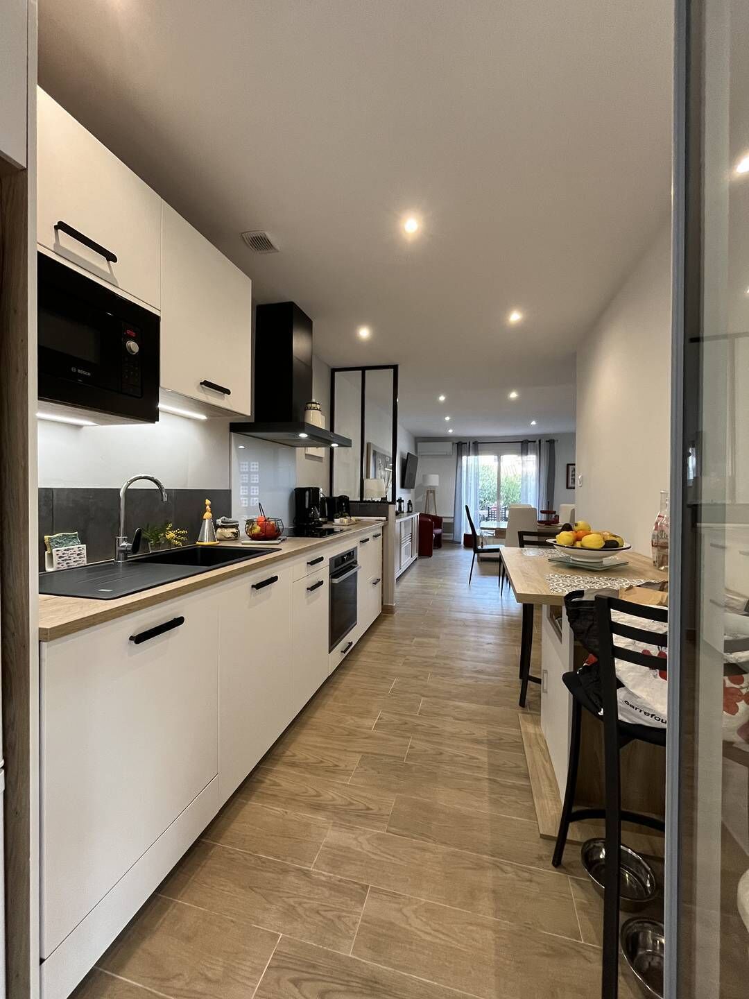 A modern kitchen with white cabinetry, a black microwave, and a dining area with a table and chairs.