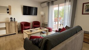A modern living room with a sofa, two red chairs, a coffee table, and a TV on the wall. - Charming single-story villa with 3 bedrooms, tastefully decorated, beautiful exterior. (CANET PLAGE)