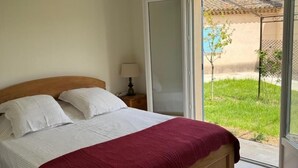 Un dormitorio con cama, mesita de noche, lámpara y puerta corrediza de vidrio que da a un jardín.