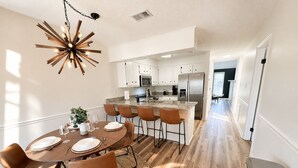 A modern kitchen with white cabinets, a stainless steel refrigerator, and a dining area with a round table and chairs. - Juniper: 3 bedroom w/ pool (Martinez)