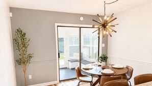 A dining area with a round table, chairs, a chandelier, and a view through a glass door. - Juniper: 3 bedroom w/ pool (Martinez)