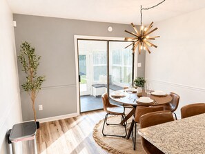 A dining area with a round table, chairs, a chandelier, and a view through a glass door. - Juniper: 3 bedroom w/ pool (Martinez)