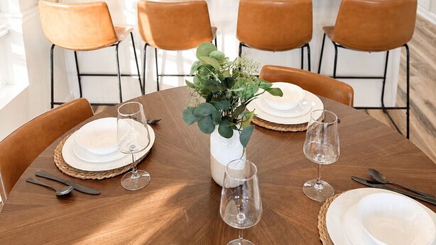 A modern kitchen with white cabinets, a granite countertop, and a wooden dining table set for six with chairs. - Juniper: 3 bedroom w/ pool (Martinez)
