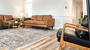 A living room with a brown leather sofa, a black leather armchair, a patterned rug, and a wooden coffee table. - Juniper: 3 bedroom w/ pool (Martinez)