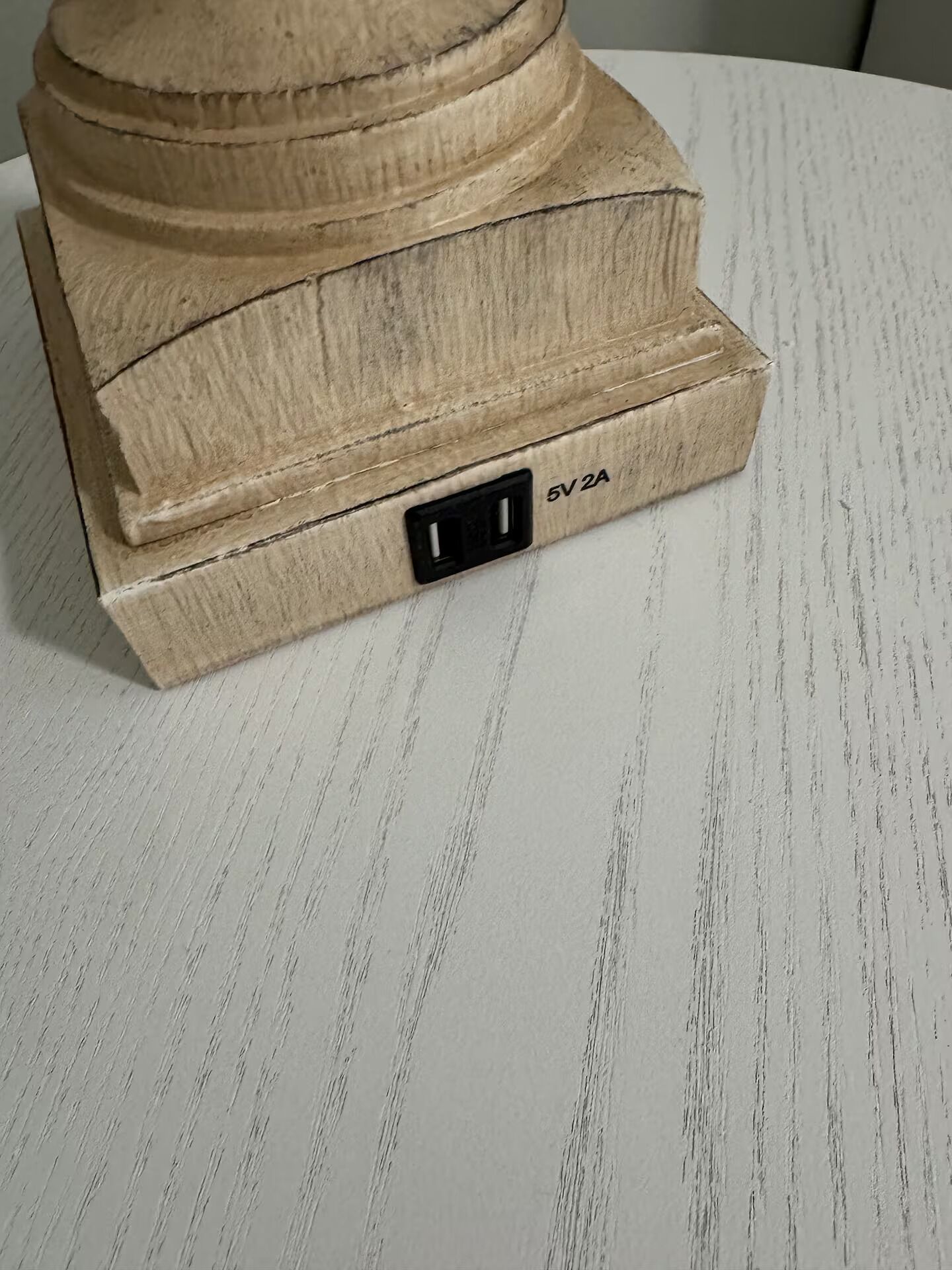 A wooden object with a 5V 2A power outlet on a white textured surface.