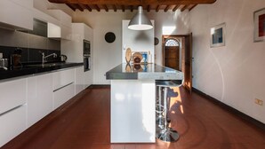 A modern kitchen with white cabinets, a central island, and a hanging pendant light. - Villa Charming on the Hills | Mixed of Authentic and Modern Tuscan Style (Siena)