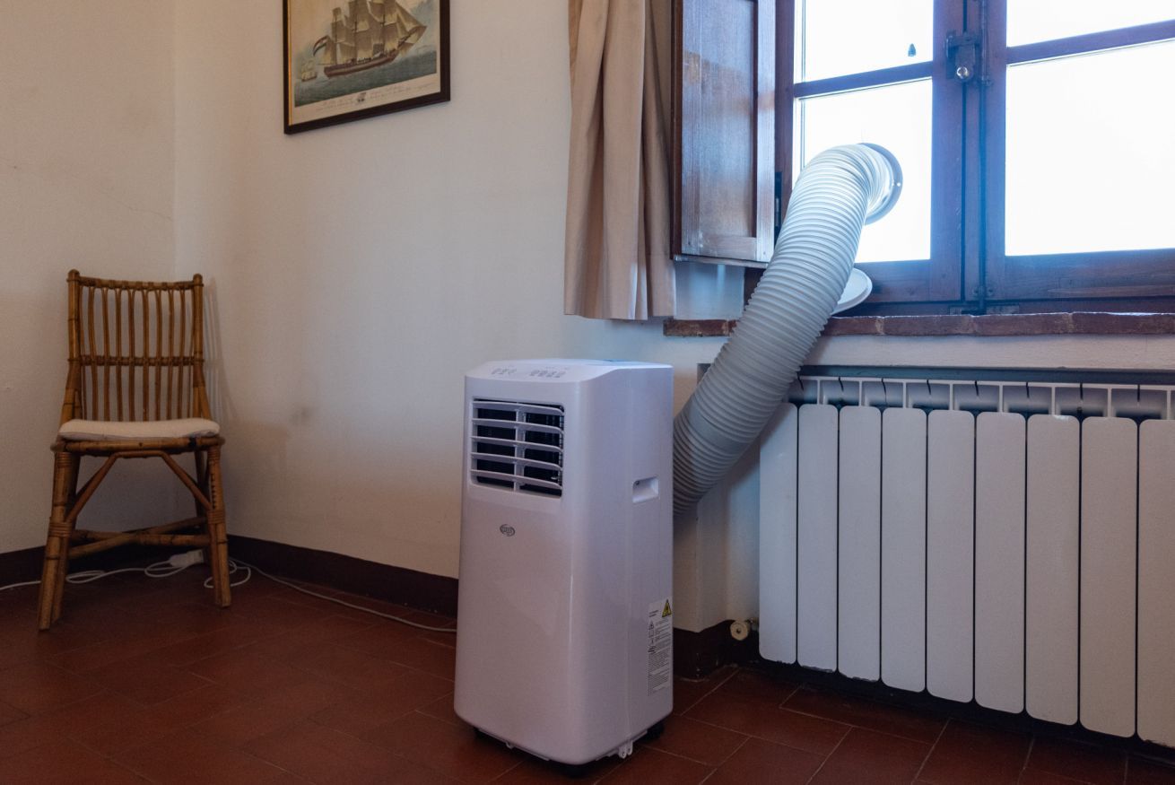 Una habitación con calefactor portátil, una ventana con cortinas, una silla de mimbre y un radiador.
