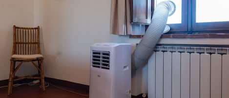 Una habitación con calefactor portátil, una ventana con cortinas, una silla de mimbre y un radiador.