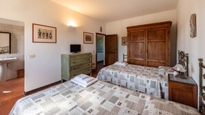 Quarto com duas camas, cômoda, televisão e guarda-roupa.