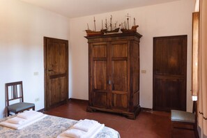 Quarto com um armário de madeira grande, duas portas, uma cama com colcha estampada e uma cadeira.