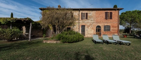 Un bâtiment rustique en pierre, doté d’un toit en tuiles, d’un petit jardin avec une pelouse et de quatre chaises longues à rayures.