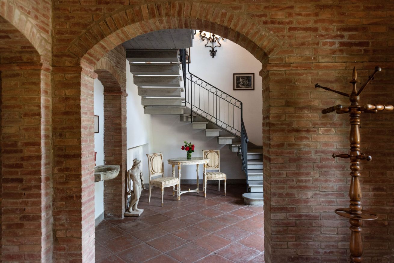 Una escalera con barandilla metálica que sube a un piso superior, una mesa con sillas y un objeto decorativo en la pared.