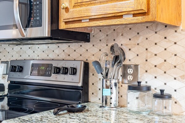 A kitchen with a stainless steel stove, a microwave, wooden cabinets, a hexagonal tile backsplash, and a utensil holder. - Cartersville Home with Basement Media Room & Yard (Cartersville)